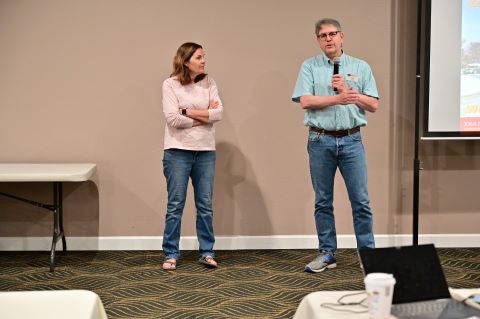 A man with a microphone introduces a woman standing next to him.